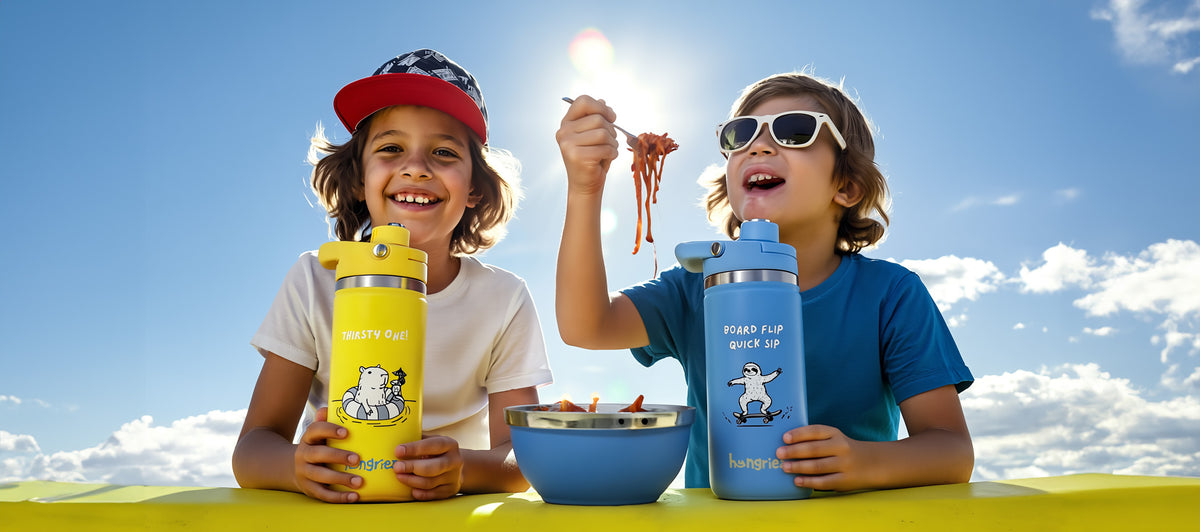 Two children enjoying ice cream with yellow and blue hungriez water bottles and thermos against a blue sky.