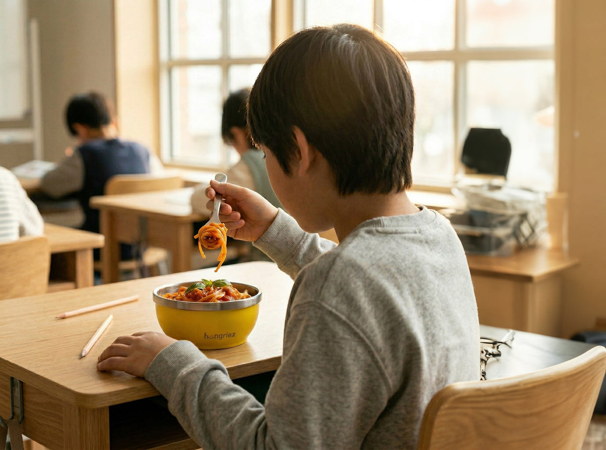 a kid eating a red sauce pasta from a hungriez in a classroom