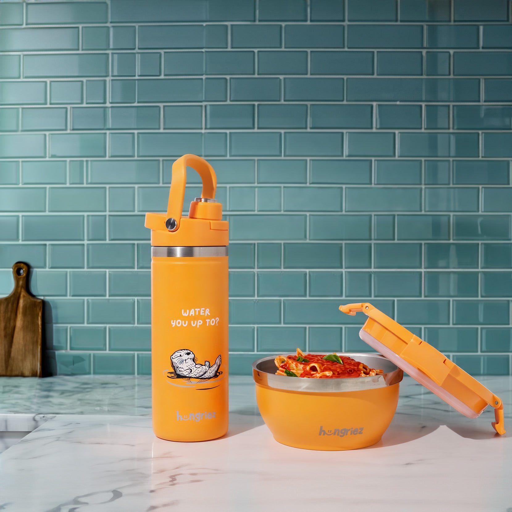 Orange water bottle and bowl set on a kitchen counter with a teal tiled wall background.