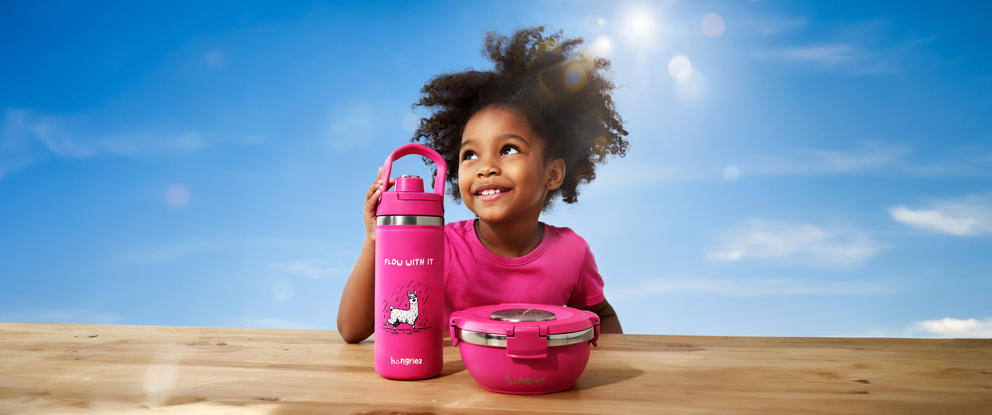 Child holding pink water bottle and lunch box against a blue sky